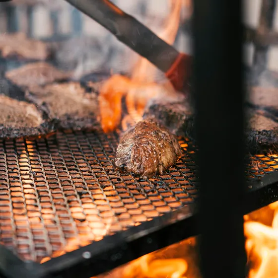 Chuleta a la brasa sobre parrilla de barras, con el fuego vivo debajo