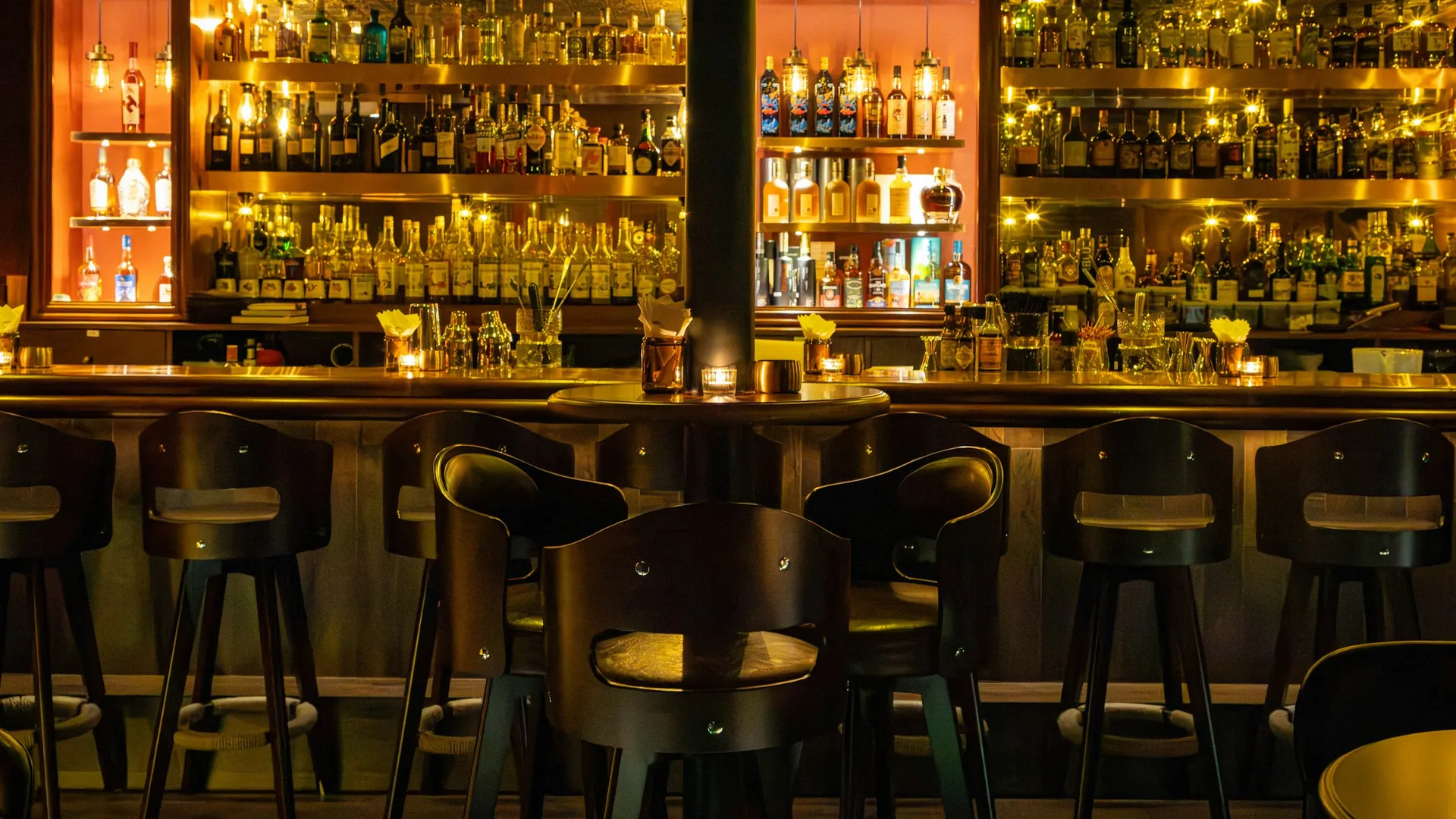 Barra de un bar de noche, con luz cálida y botellas iluminadas en las estanterías